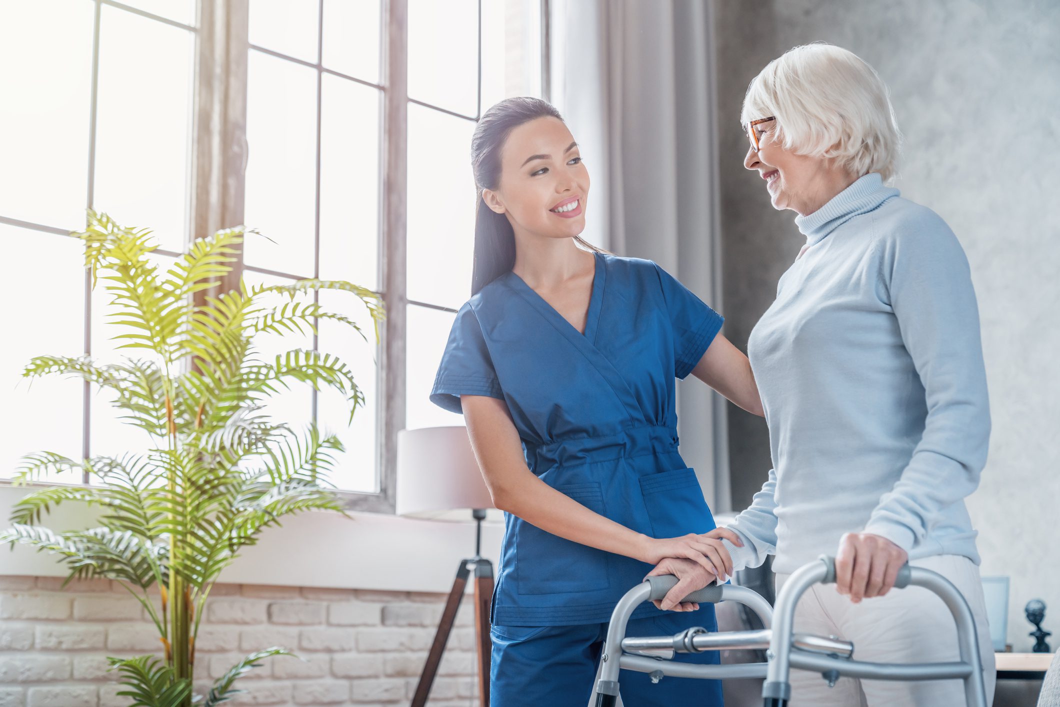 Female asian nurse helping senior woman to walk with walker at home